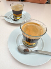 Close-up of two glasses of cremaet, a traditional Valencian coffee drink made with espresso, rum, sugar, and lemon zest. Served on white saucers with coffee beans on the spoon.