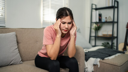 Fototapeta premium Woman experiencing intense headache pain stress discomfort sitting on sofa at home seeking relief overwhelming fatigue unwell