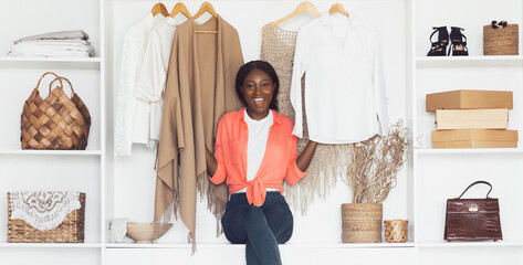 Shopaholic. Joyful African American Lady Sitting In Wardrobe Among Trendy Clothes Smiling To Camera At Home. Sucessful Shopping, Fashion And Style Concept. Full Length Shot