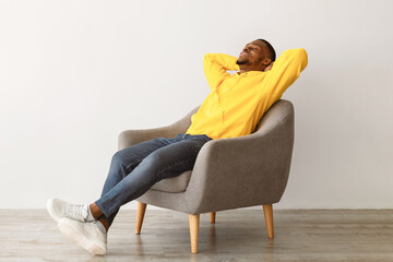 Black Millennial Guy Relaxing Sitting In Comfortable Chair Holding Hands Behind Head Resting With...