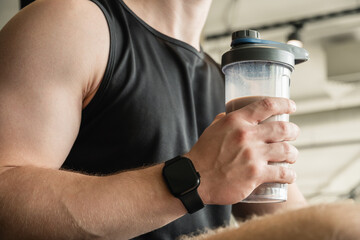 Young bodybuilder and sporty man with protein shake while working out at gym or fitness center. Health care and workout.