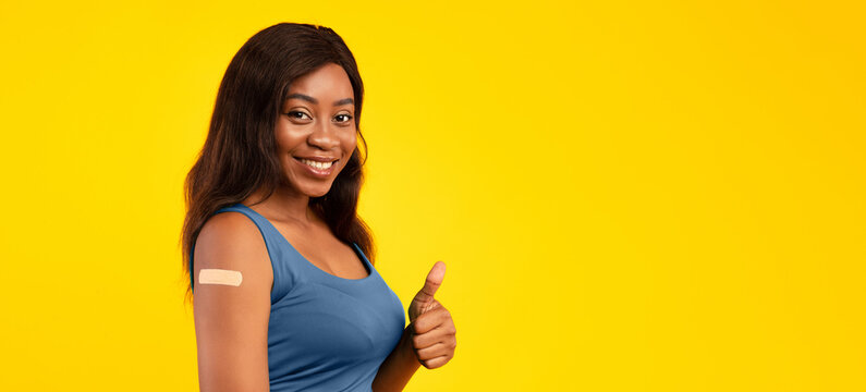 I Like Vaccination. Vaccinated Black Female Showing Thumbs Up And Arm With Plaster After Antiviral Vaccine Shot For Virus Prevention On Yellow Studio Background. Coronavirus Immunization. Panorama