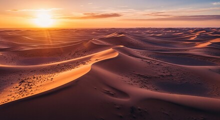 A vast desert landscape with rolling sand dunes under a vibrant sunset. The sky displays warm hues of orange and purple, creating a serene atmosphere.