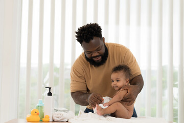 Obraz premium African American father wearing newborn baby diaper on white towel after taking shower. Father changing newborn baby diaper at home