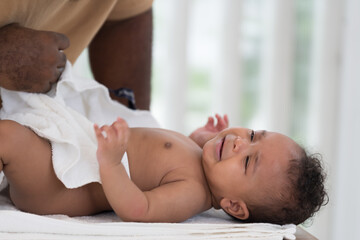 African American father wearing newborn baby diaper on white towel after taking shower. Father changing newborn baby diaper at home