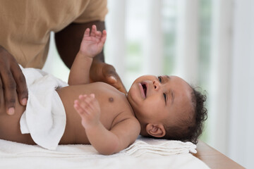 African American father wearing newborn baby diaper on white towel after taking shower. Father...