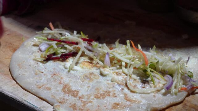 A wrap or egg roll being prepared and adding ketchup salads and salts before famous and popular street food in India