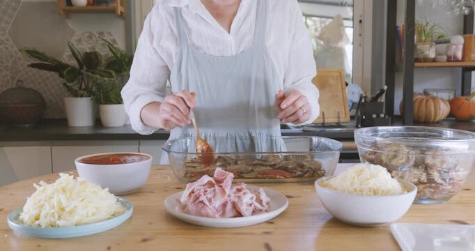 Woman prepares eggplant parmigiana, putting tomato sauce on fried slices of eggplant into lasagna pan