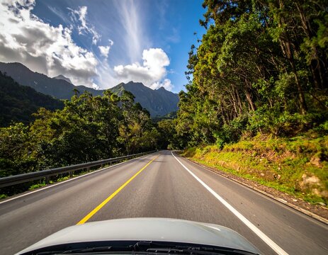 Road to Adventure: A scenic highway winds its way through a lush, green landscape, leading toward distant mountains under a bright blue sky with scattered clouds. - Powered by Adobe