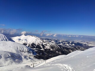 A vast snow-covered panorama from Kasprowy Wierch in Poland, featuring rugged white mountain peaks against a brilliant deep blue winter sky.