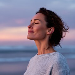 A smiling woman practicing mindfulness meditation on a beach at sunset with calm waves and pastel sky