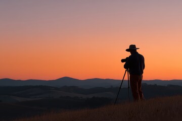A photographer setting up equipment to capture a sunrise landscape over rolling hills