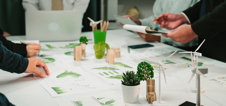 A diverse team collaborates on innovative business solutions in a modern workspace. Green elements and charts highlight a focus on sustainability and growth strategies. SACTR