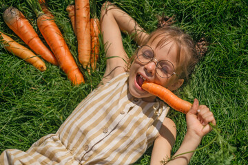 A funny girl with glasses is lying in the grass eating carrots, enjoying her vacation.