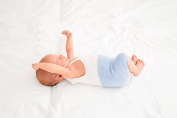 A cute newborn baby in bed wakes up pulling himself up while waking up. Strong healthy sleep of the child.