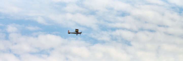 Small airplane navigates through partly cloudy sky. Light blue background contrasts with white clouds, capturing sense of freedom and exploration. Photographed from low angle