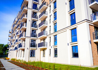 Modern Residential Building With Balconies and Landscaped Garden in Sunny Weather. New residential structure features multiple balconies and windows, surrounded by neatly kept garden  clear blue sky
