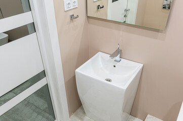 Modern bathroom detail: pedestal sink with chrome faucet, mirror, and a white door with glass panels. Soft beige wall color