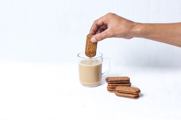 Hand dipping crunchy biscuit into a glass of hot milk tea with stack of cookies. breakfast and snack concept