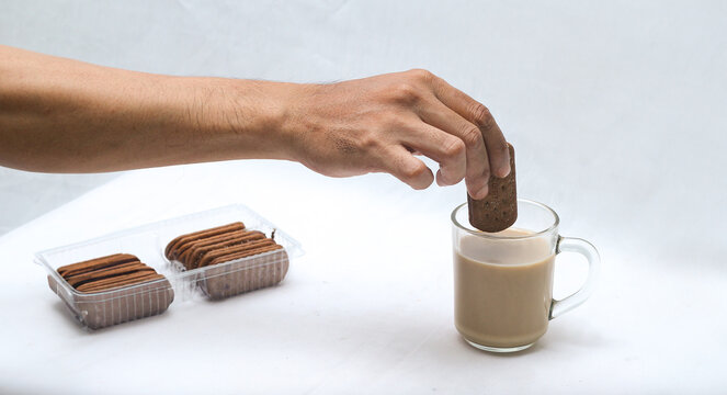 Hand dipping crunchy biscuit into a glass of hot milk tea with stack of cookies. breakfast and snack concept