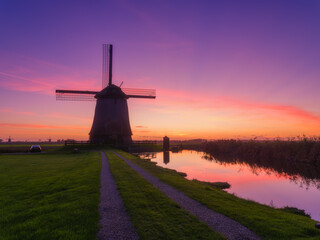 Windmill and road in the Netherlands. A historic building in the Dutch countryside. Reflections on the surface of water. Postcards, background, wallpaper.