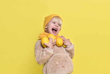 Little blue boy of 3 years old with a cap and a scarf holds a lemon in his hands