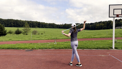 Young woman holding jump rope on outdoor sports court, preparing for cardio workout and fitness training, healthy lifestyle concept with athlete in activewear standing on red track field under blue
