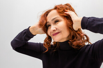 beautiful 60 years old mature woman with curly red hair smiling confidently while touching her hair.