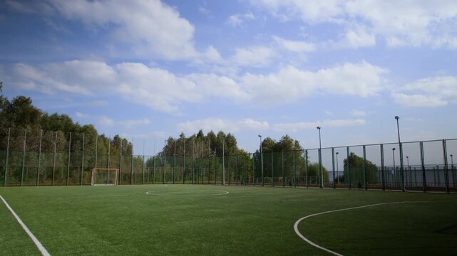 Tilt shot of empty football pitch covered with green turf with touchlines, metal goal placed on it