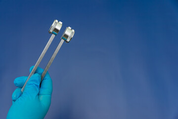 Blue Gloved Hands Holding tuning fork On blue Background, medical instruments in the hands of a doctor
