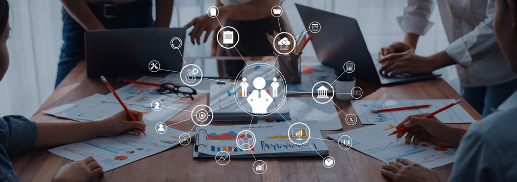 A dynamic business meeting scene showcasing professionals collaborating with laptops, hands engaged in discussions, and detailed charts on a table, representing teamwork and strategy. Trope