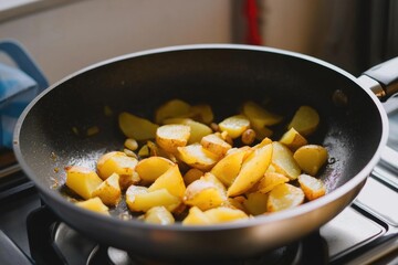 Golden brown potato wedges sizzling in a non-stick pan on a stovetop