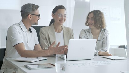 Professional team analyzing data on laptop, sharing insights during collaborative office meeting, highlighting workplace synergy and strategic planning. Business people concept