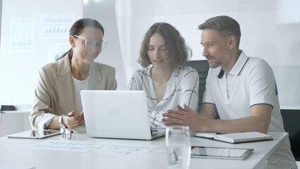 Business professionals reviewing marketing analytics on laptops, working together strategically in contemporary workplace with minimalist interior design and collaborative atmosphere