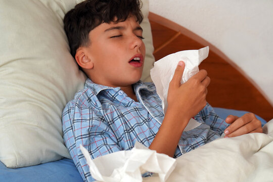 child in pajamas sick in bed with a cough and a tissue
