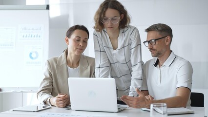 Business team collaborating and analyzing data on a laptop during a dynamic office meeting, uniting efforts to reach shared objectives and drive successful outcomes together