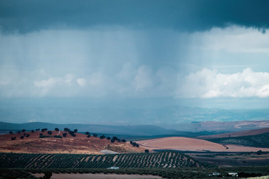 Dark rain clouds loom over patchwork farmland and rolling hills, capturing the dramatic atmosphere of changing weather in the countryside.