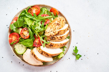 Green salad with grilled chicken meat at black table.