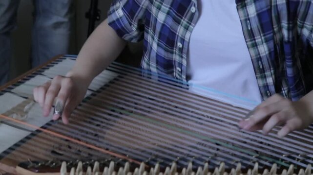 Close-up of a musician's hands skillfully playing a traditional stringed instrument, likely a cymbalom or similar zither, using picks to strike the strings.

