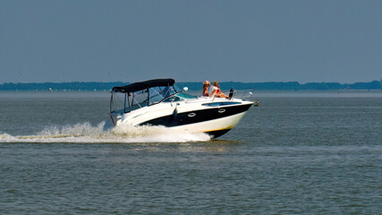 Modern motor yacht with people enjoying a summer ride on calm lake water. Concept of leisure, vacation, freedom, and luxury lifestyle.
