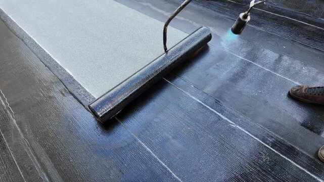 Roofer applying torch to bitumen membrane on torch down roof