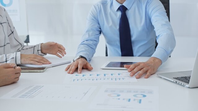 Business people analyzing financial charts, graphs on tablet and laptop, collaborating closely during strategic planning session in office