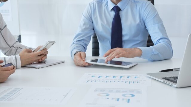 Business colleagues strategizing in modern workspace, reviewing financial analytics on digital devices, sharing insights through collaborative teamwork and data driven discussion - Powered by Adobe