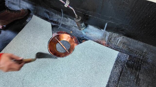 Roofer applying torch to bitumen membrane on torch down roof