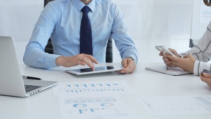 Professional team collaborating, reviewing financial data on digital devices during strategic meeting in contemporary corporate workspace, focusing on performance metrics