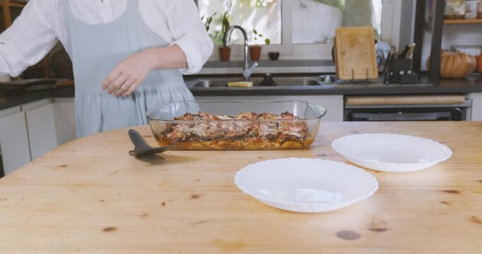 Woman putting portion of eggplant parmigiana on plate from lasagna pan