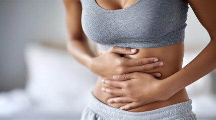 Young woman clutching lower abdomen with both hands, wincing from intense stomach or menstrual pain, depicting discomfort, cramps, illness, or digestive distress at home