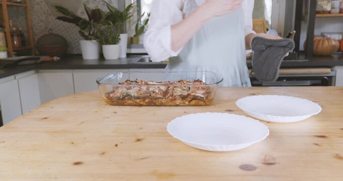 Woman putting portion of eggplant parmigiana on plate from lasagna pan
