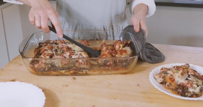 Woman putting portion of eggplant parmigiana on plate from lasagna pan