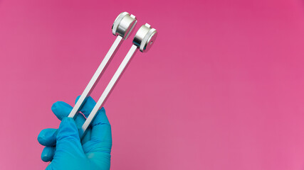 Blue Gloved Hands Holding tuning fork On pink Background, medical instruments in the hands of a doctor